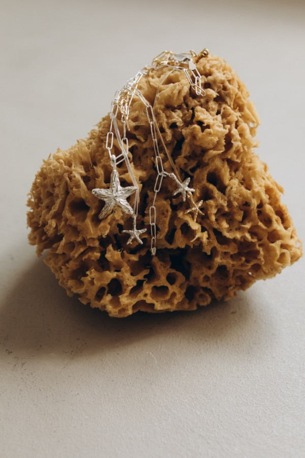 Stylizowane zdjęcie z gąbką morską – mini zawieszka STARFISH GOLD w towarzystwie srebrnych odpowiedników i różnych typów łańcuszków.