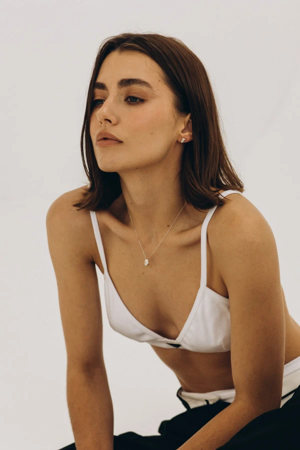 Modelka w białym topie prezentuje naszyjnik SPOT SILVER – minimalistyczna stylizacja, biżuteria eksponowana na dekolcie.